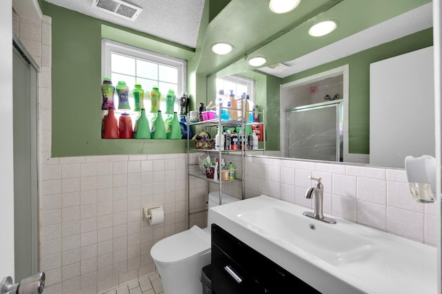 bathroom featuring tile patterned floors, vanity, tile walls, toilet, and a shower with shower door