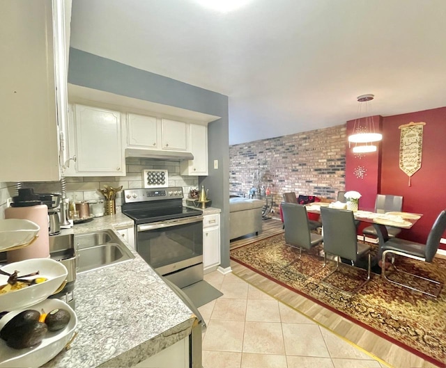 kitchen featuring stainless steel electric range, brick wall, light tile patterned floors, white cabinetry, and decorative light fixtures