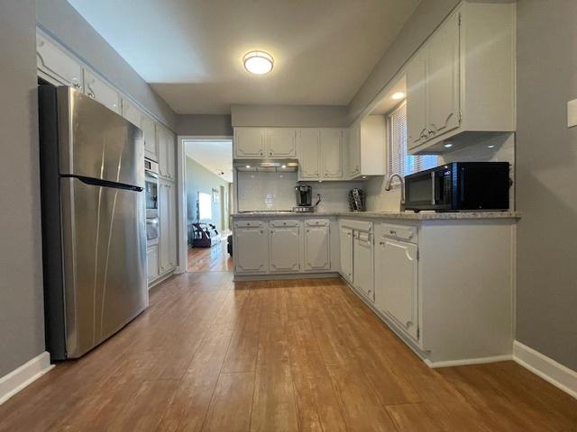 kitchen with black appliances, backsplash, white cabinets, and sink