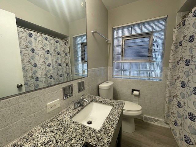 bathroom with hardwood / wood-style floors, vanity, toilet, tile walls, and walk in shower