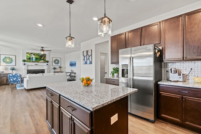 kitchen with a center island, a fireplace, a ceiling fan, light wood-type flooring, and stainless steel fridge with ice dispenser