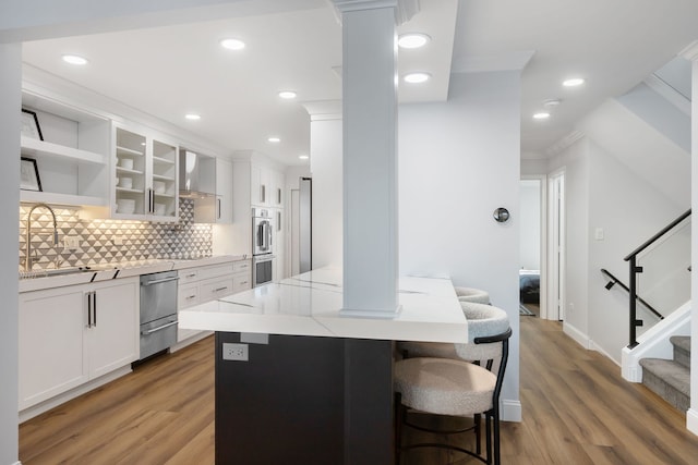 kitchen featuring sink, a breakfast bar area, white cabinetry, backsplash, and hardwood / wood-style floors