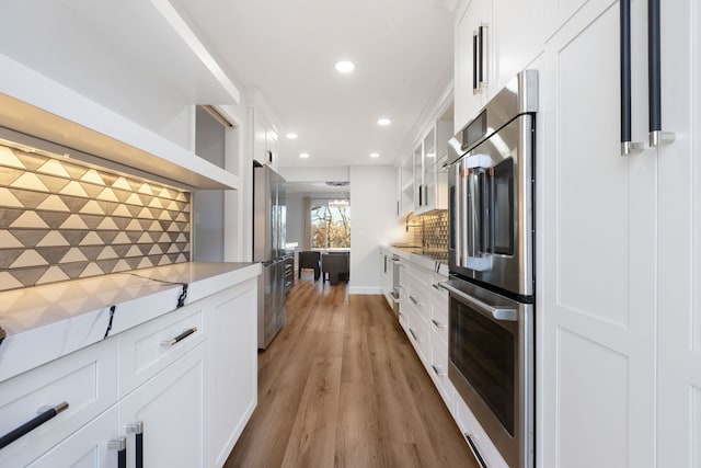 kitchen with tasteful backsplash, light wood-type flooring, fridge, stainless steel fridge, and white cabinets