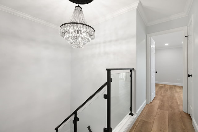 hallway with baseboards, light wood-style flooring, ornamental molding, a notable chandelier, and an upstairs landing