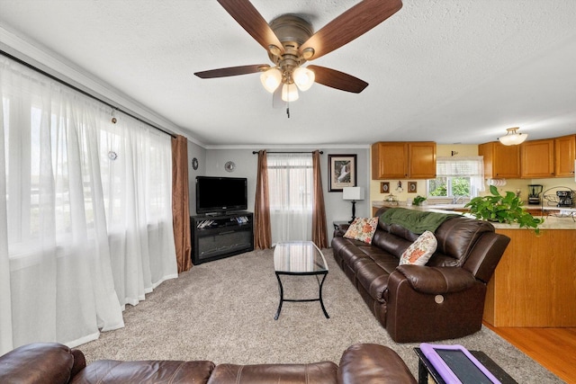 living room featuring ceiling fan, light colored carpet, a textured ceiling, and crown molding