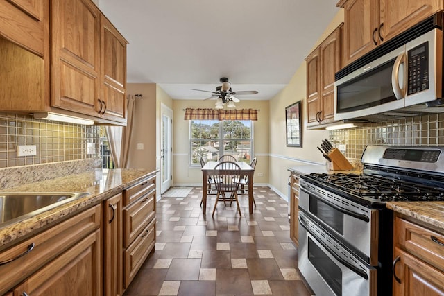 kitchen featuring light stone countertops, stainless steel appliances, tasteful backsplash, and ceiling fan