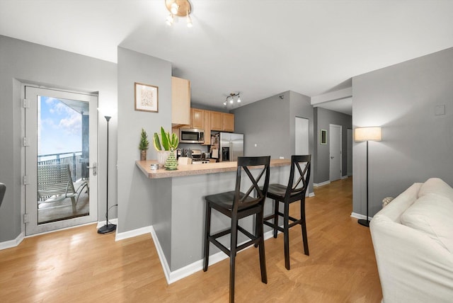 kitchen featuring a breakfast bar, light wood-type flooring, light brown cabinetry, appliances with stainless steel finishes, and kitchen peninsula