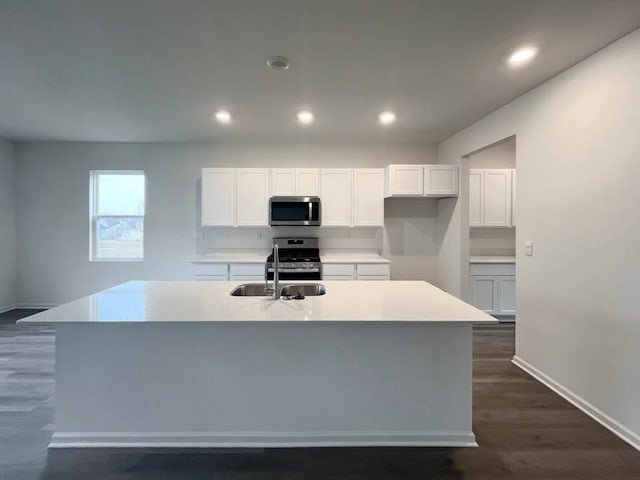 kitchen featuring appliances with stainless steel finishes, sink, white cabinets, dark wood-type flooring, and a center island with sink