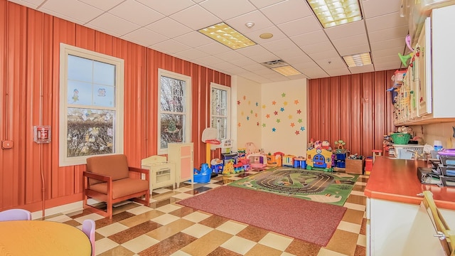 game room with a paneled ceiling and wooden walls