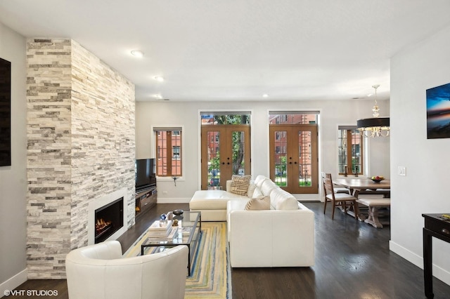 living room featuring a chandelier, a stone fireplace, dark wood-type flooring, and french doors