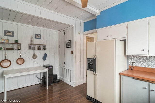 kitchen featuring white cabinets, white refrigerator with ice dispenser, and wooden walls