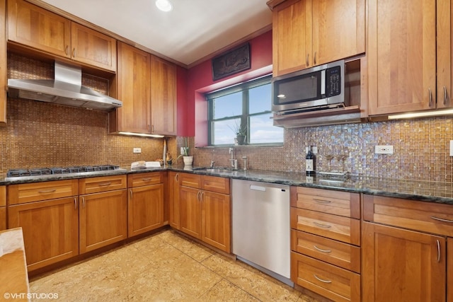 kitchen featuring appliances with stainless steel finishes, sink, dark stone countertops, decorative backsplash, and wall chimney range hood