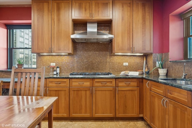 kitchen featuring tasteful backsplash, stainless steel gas stovetop, sink, dark stone countertops, and wall chimney range hood