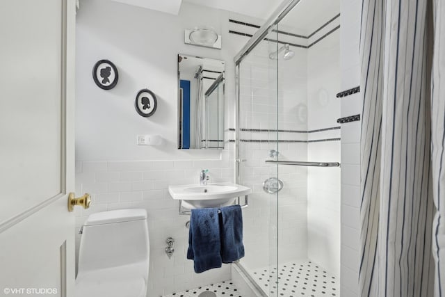 bathroom with toilet, a shower with shower door, sink, and tile walls