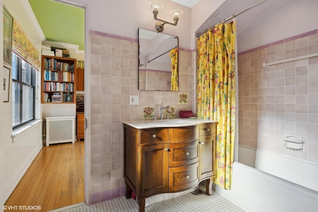 bathroom featuring radiator, wood-type flooring, tile walls, shower / bath combination with curtain, and vanity