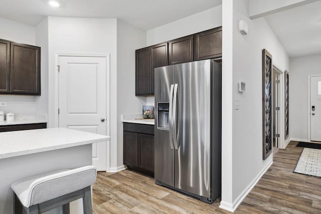 kitchen with a breakfast bar area, dark brown cabinets, wood-type flooring, and stainless steel refrigerator with ice dispenser