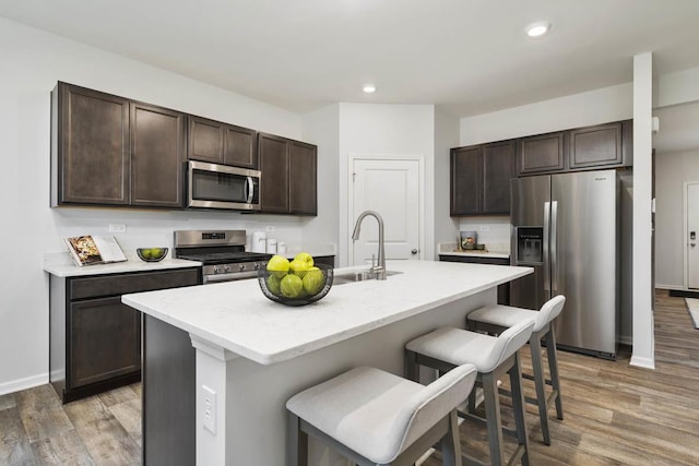 kitchen with dark brown cabinets, a kitchen bar, a kitchen island with sink, and appliances with stainless steel finishes