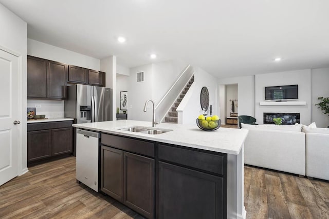 kitchen with dark hardwood / wood-style floors, sink, appliances with stainless steel finishes, and an island with sink