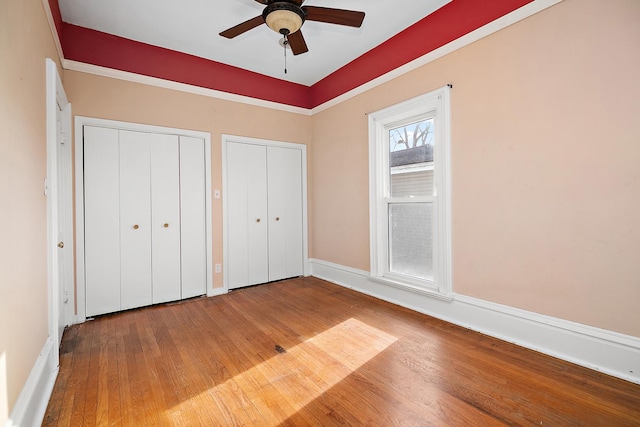 unfurnished bedroom featuring ceiling fan, hardwood / wood-style floors, and two closets