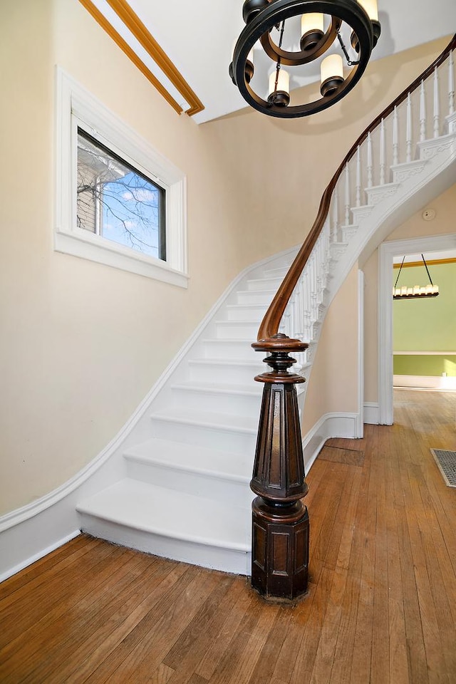 stairway featuring crown molding, hardwood / wood-style floors, and an inviting chandelier