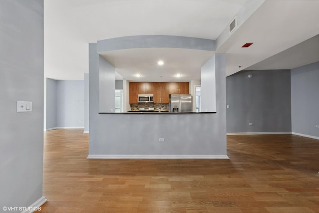 kitchen with light hardwood / wood-style floors, kitchen peninsula, stainless steel appliances, and tasteful backsplash