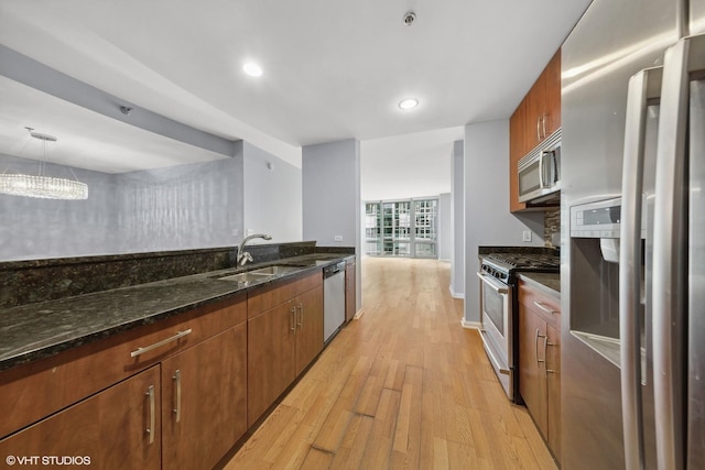 kitchen featuring light wood-type flooring, stainless steel appliances, sink, pendant lighting, and dark stone countertops