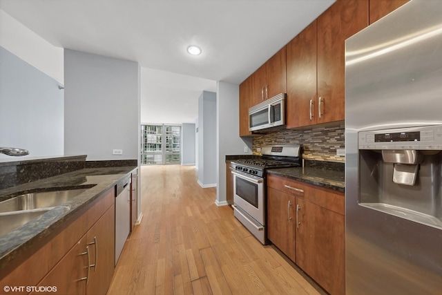 kitchen with backsplash, dark stone counters, stainless steel appliances, sink, and light hardwood / wood-style flooring