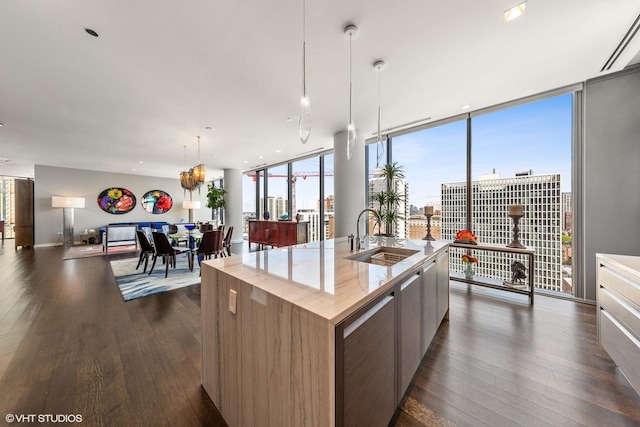 kitchen with a kitchen island with sink, dark wood-type flooring, sink, a wall of windows, and hanging light fixtures