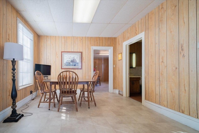 dining space with wood walls and a drop ceiling