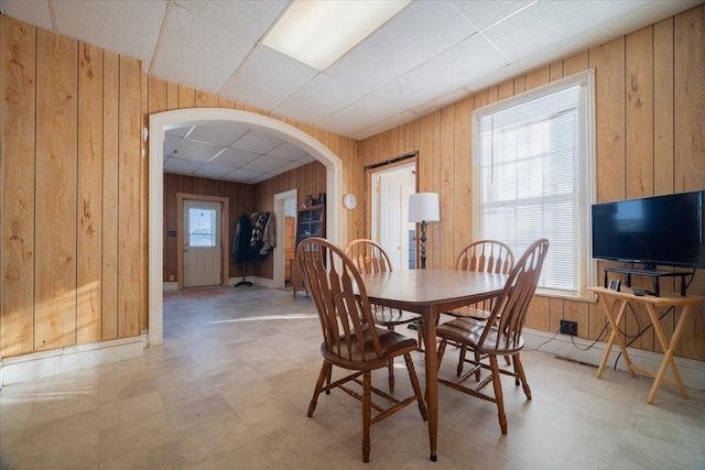 dining area with wood walls and a drop ceiling