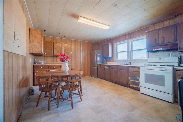 kitchen featuring sink, gas range gas stove, stainless steel fridge, and wooden walls