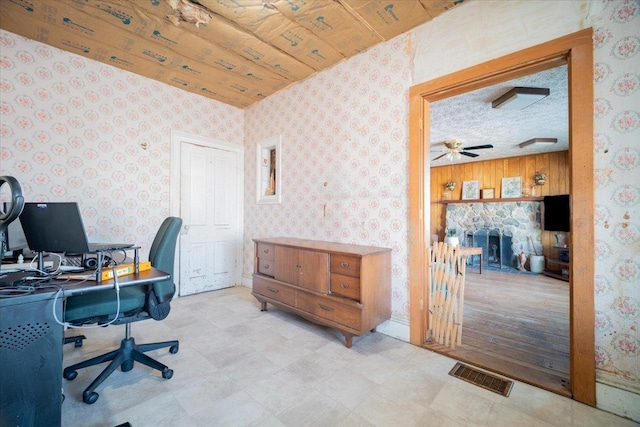 office with ceiling fan, a stone fireplace, wood walls, and a textured ceiling