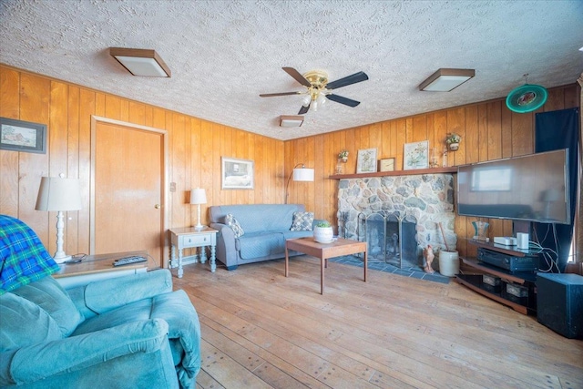 living room featuring a fireplace, ceiling fan, light hardwood / wood-style floors, and wooden walls