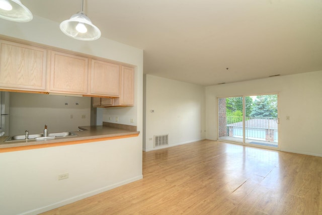 kitchen with light brown cabinetry, light wood-type flooring, decorative light fixtures, and sink