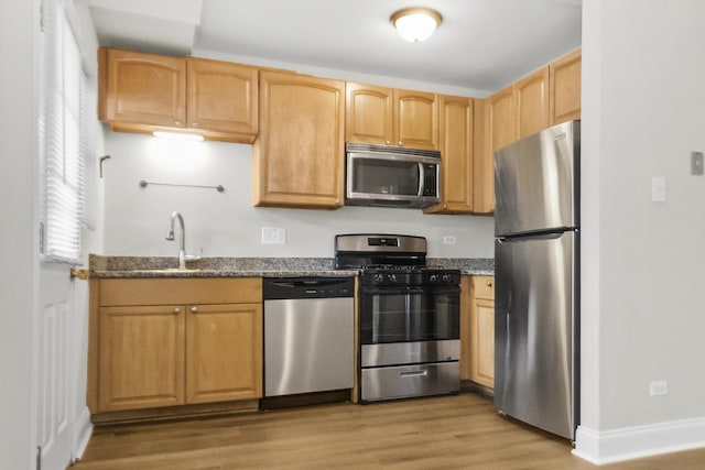 kitchen with sink, light brown cabinets, light hardwood / wood-style floors, dark stone counters, and appliances with stainless steel finishes