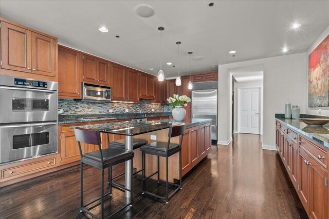 kitchen with a kitchen breakfast bar, stainless steel appliances, a kitchen island, and dark stone countertops