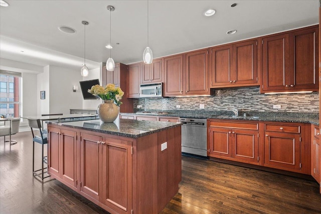 kitchen with decorative light fixtures, a kitchen island, appliances with stainless steel finishes, and dark stone counters