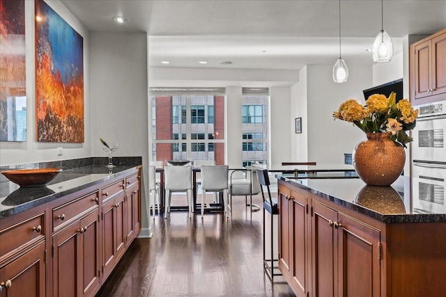 kitchen featuring dark hardwood / wood-style flooring, white double oven, dark stone countertops, a center island, and hanging light fixtures