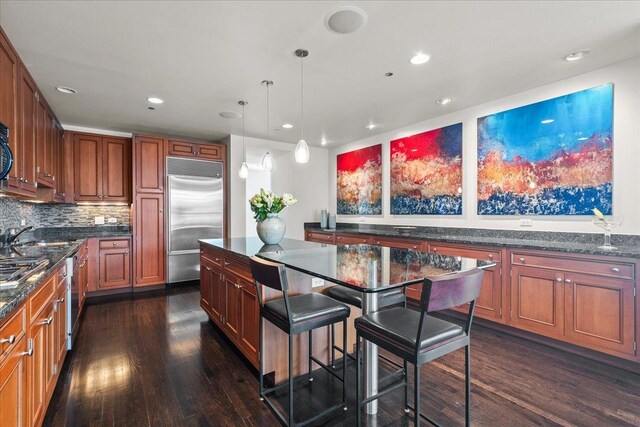 kitchen featuring backsplash, dark wood-type flooring, appliances with stainless steel finishes, decorative light fixtures, and a kitchen island