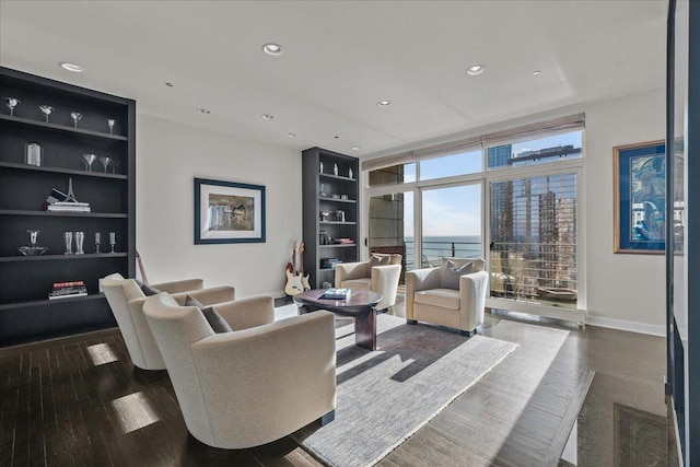 living room featuring built in shelves, dark hardwood / wood-style flooring, a water view, and a wall of windows