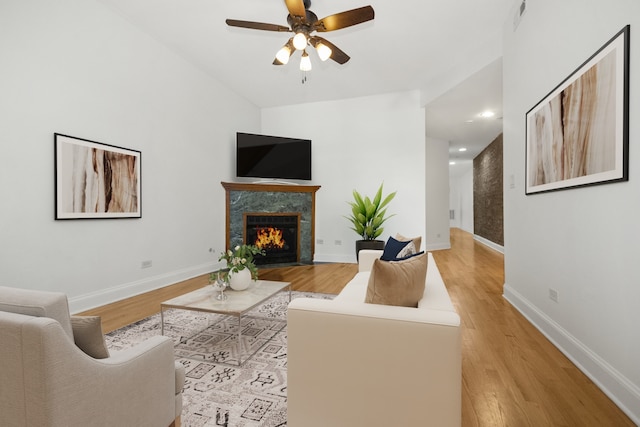 living room featuring ceiling fan, a high end fireplace, and light wood-type flooring