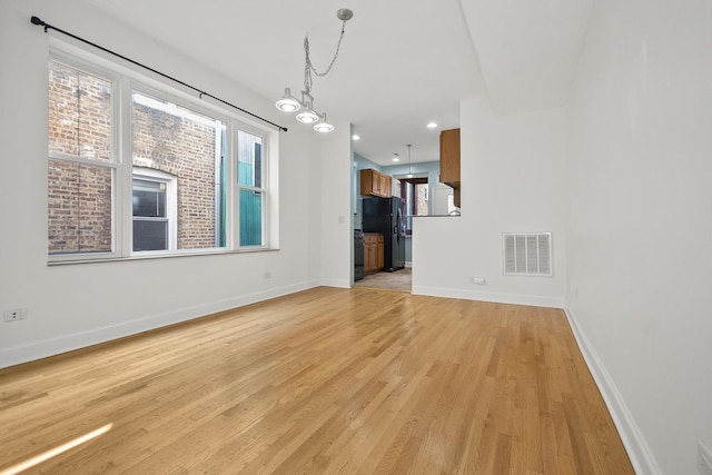 unfurnished living room featuring a chandelier and light hardwood / wood-style flooring