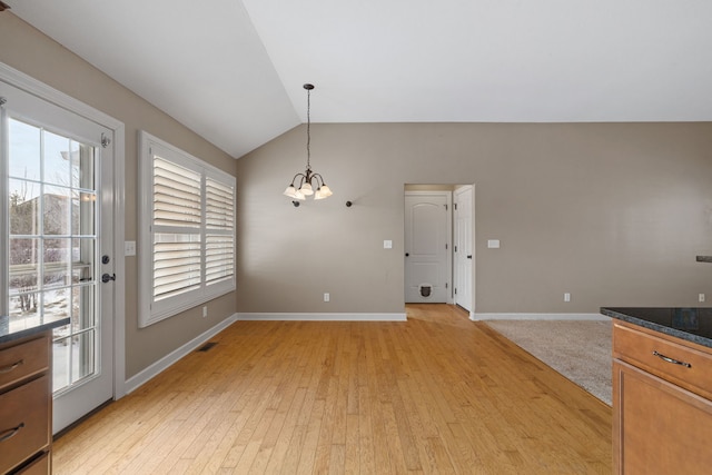 unfurnished dining area featuring light wood-type flooring, vaulted ceiling, a wealth of natural light, and a notable chandelier