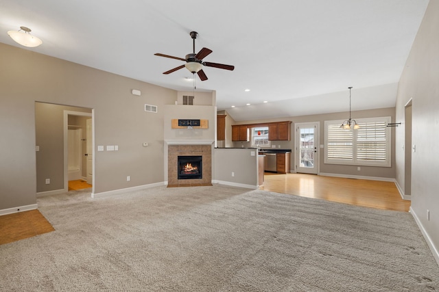 unfurnished living room featuring ceiling fan with notable chandelier, light colored carpet, and a fireplace