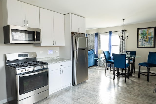 kitchen featuring white cabinets, decorative light fixtures, stainless steel appliances, and a notable chandelier