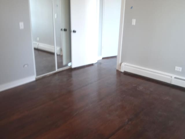 unfurnished room featuring baseboard heating and dark wood-type flooring