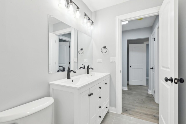 full bathroom featuring double vanity, baseboards, toilet, and a sink