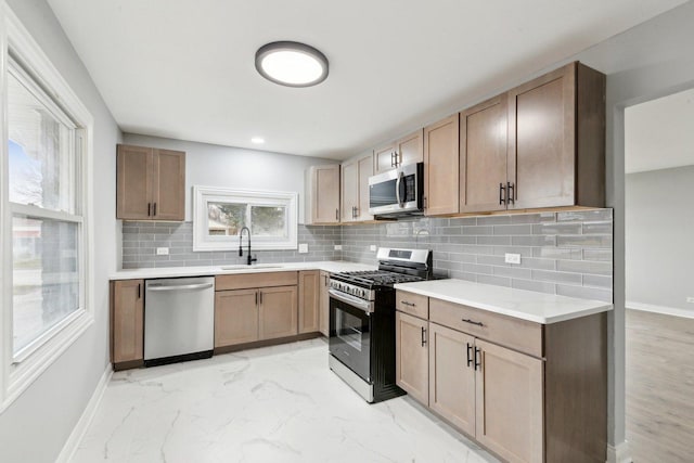 kitchen featuring tasteful backsplash, baseboards, marble finish floor, stainless steel appliances, and a sink