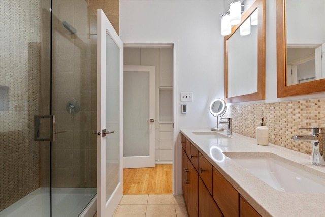 bathroom featuring tile patterned flooring, vanity, a shower with shower door, and backsplash