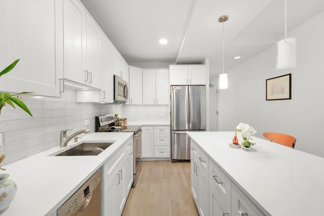 kitchen featuring appliances with stainless steel finishes, decorative light fixtures, white cabinetry, and sink